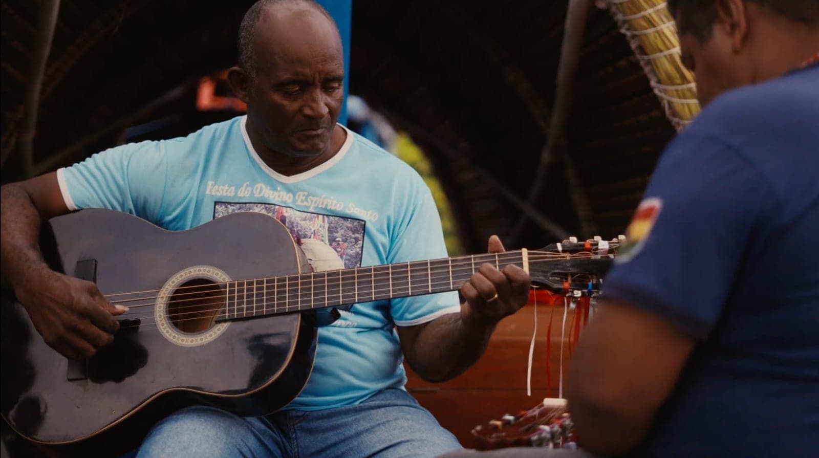 Homem de camiseta azul tocando violão.