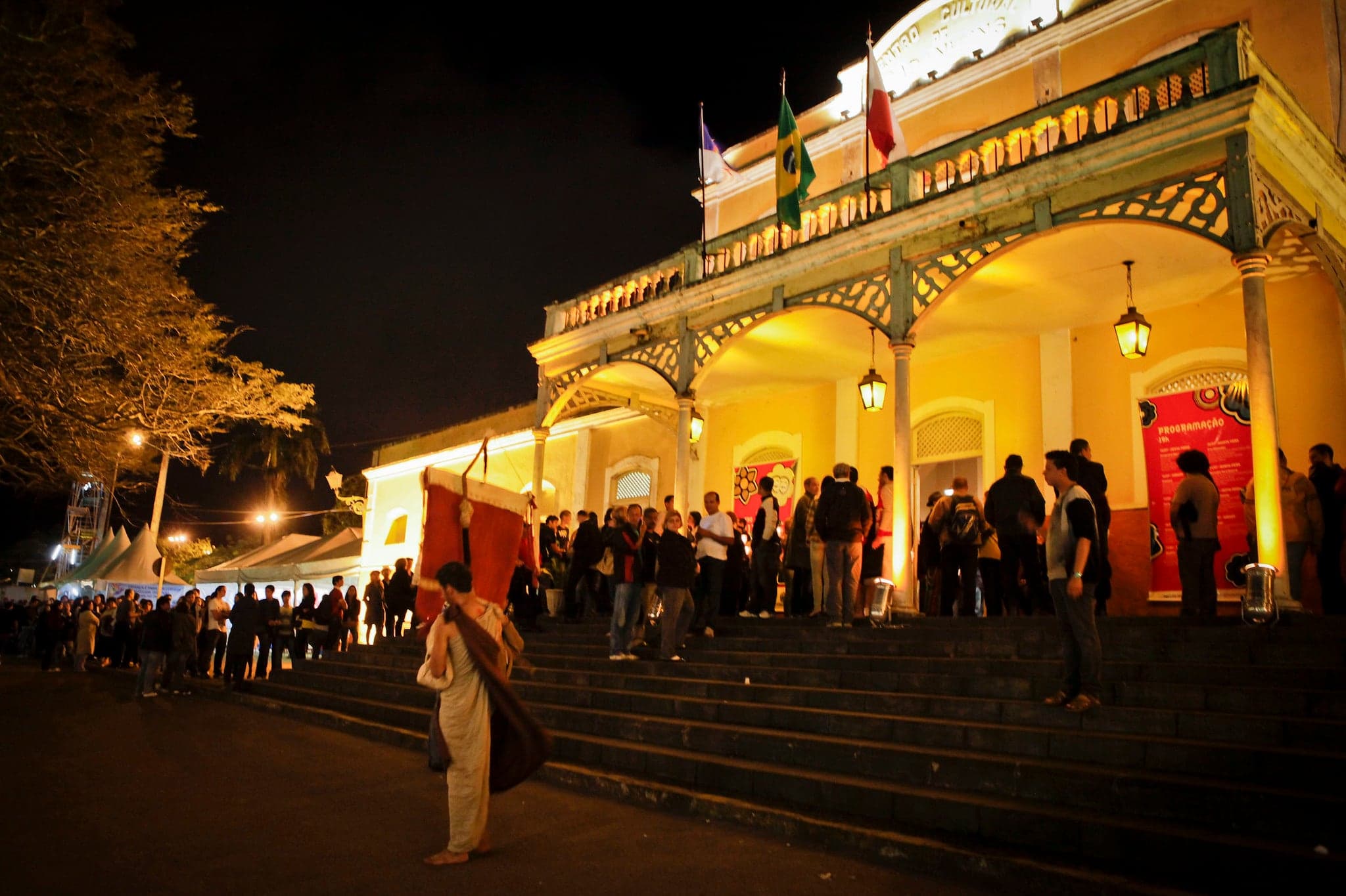 O Frei, à noite, na escadaria de um teatro iluminado, diante do público na fila.