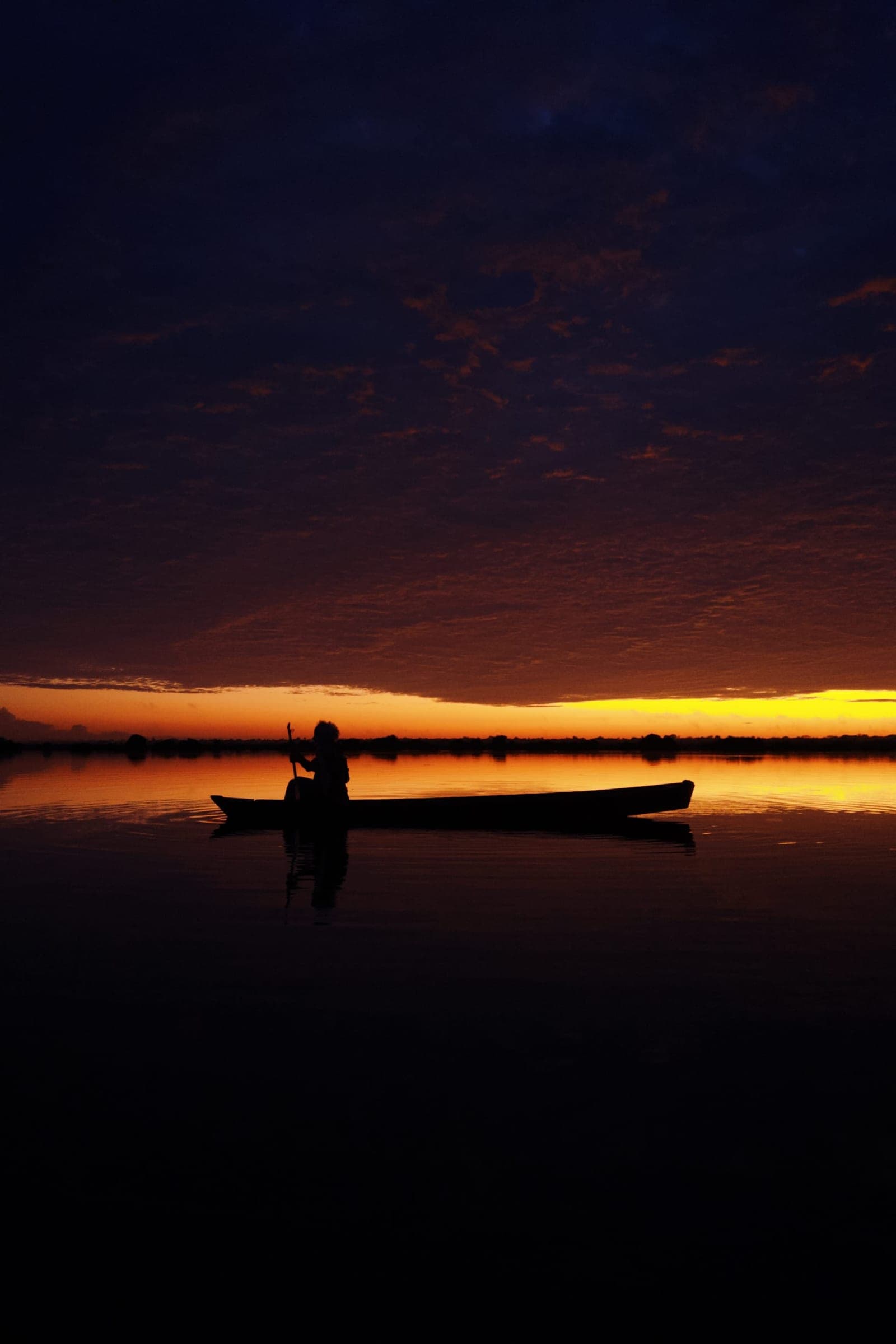Silhueta de uma canoa no lago, sob o céu laranja do pôr do sol.
