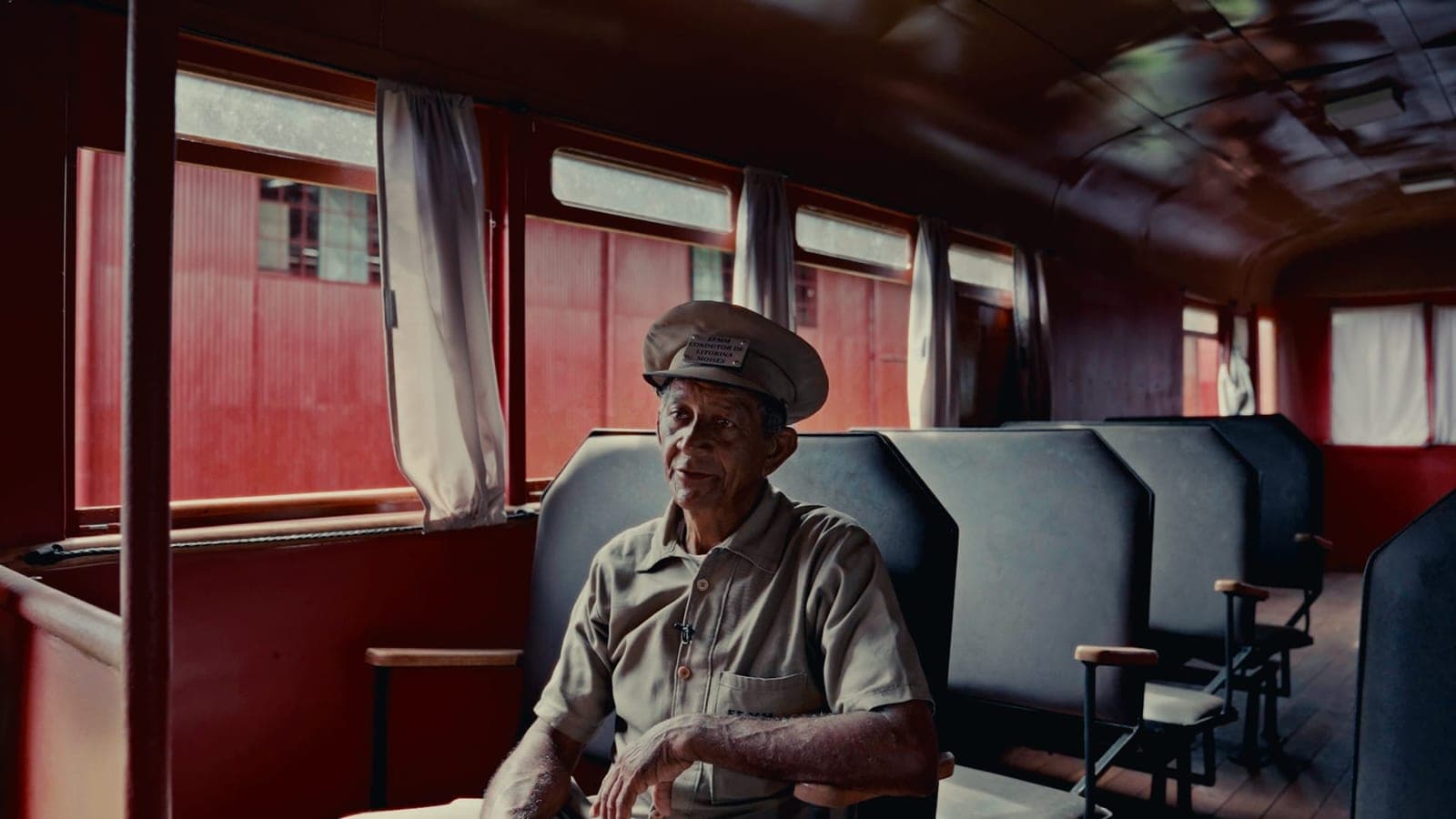 Senhor de quepe sentado no vagão de um trem antigo, de bancos azuis.