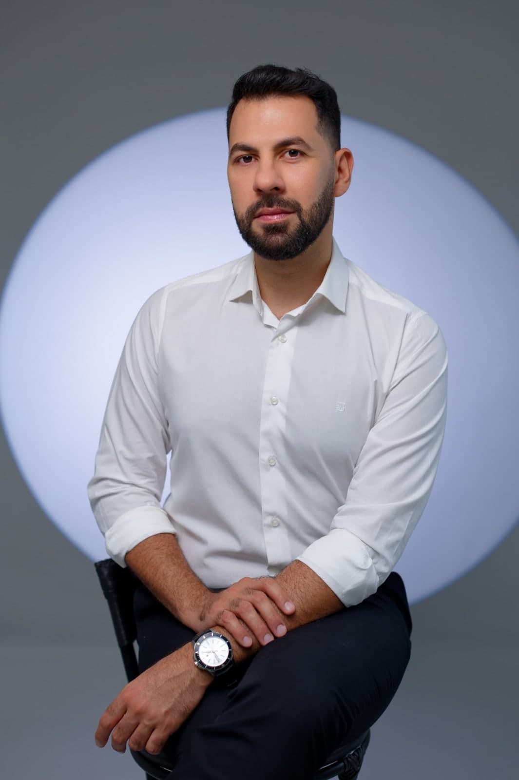 Juraci Júnior sentado, de camisa branca, diante de um círculo de luz.